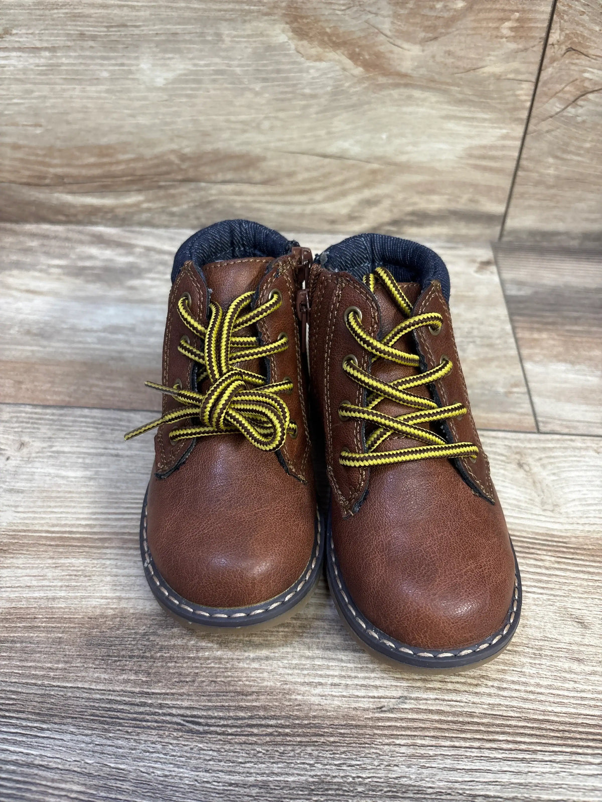 Front view of toddler brown London Fog lace-up boots with yellow-striped laces, side zipper, and stitched sole on wood floor
