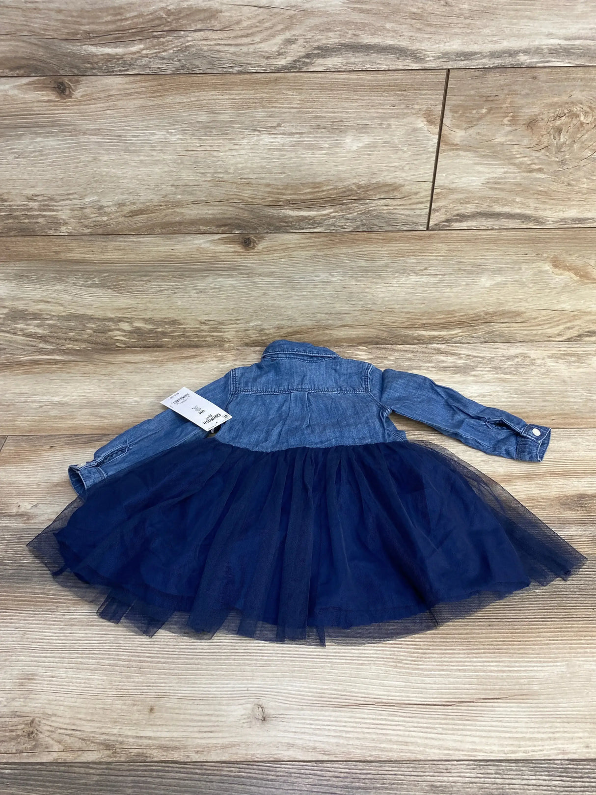 Back flat-lay of Oshkosh chambray dress showcasing navy tulle skirt and included bloomers, size 12 months, on wood floor background