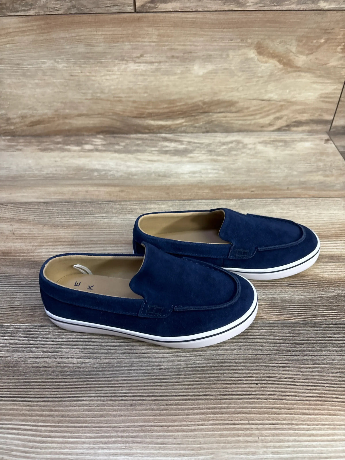 Top view of Janie & Jack blue suede slip-on sneakers showcasing white soles with a wood-grain background