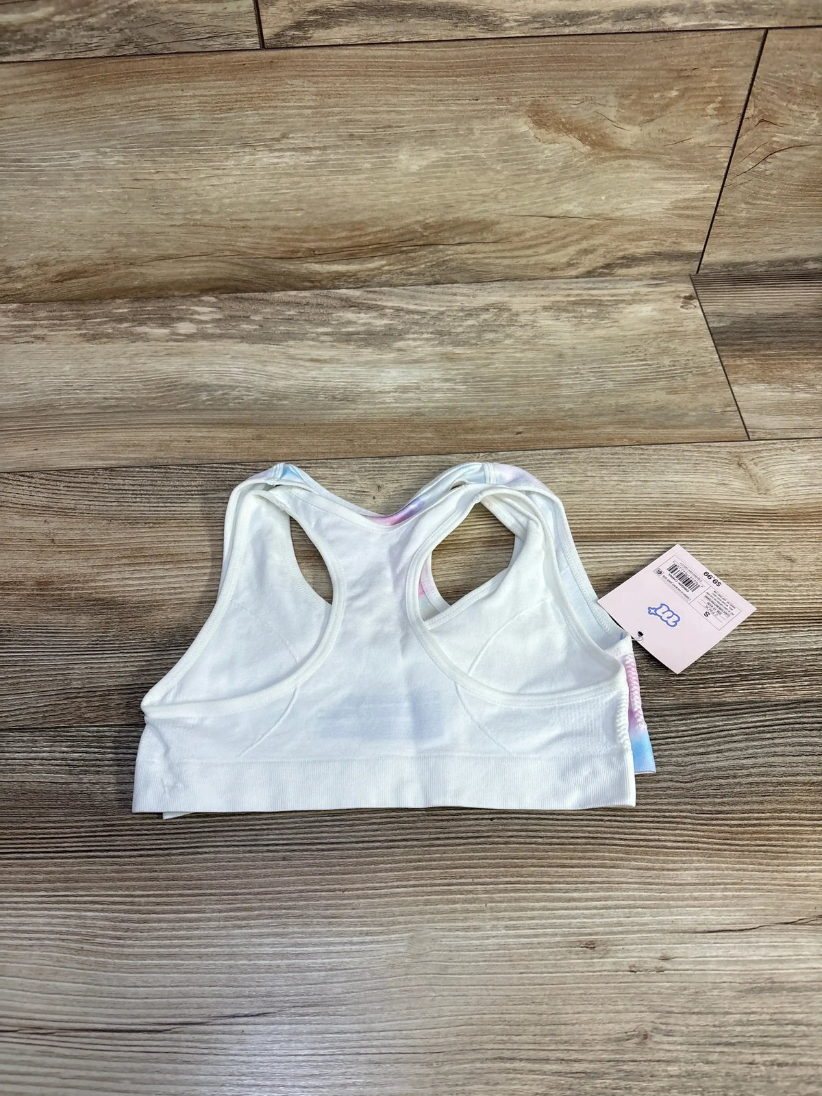 White racerback sports bra with tag on wooden floor, athletic wear product photo