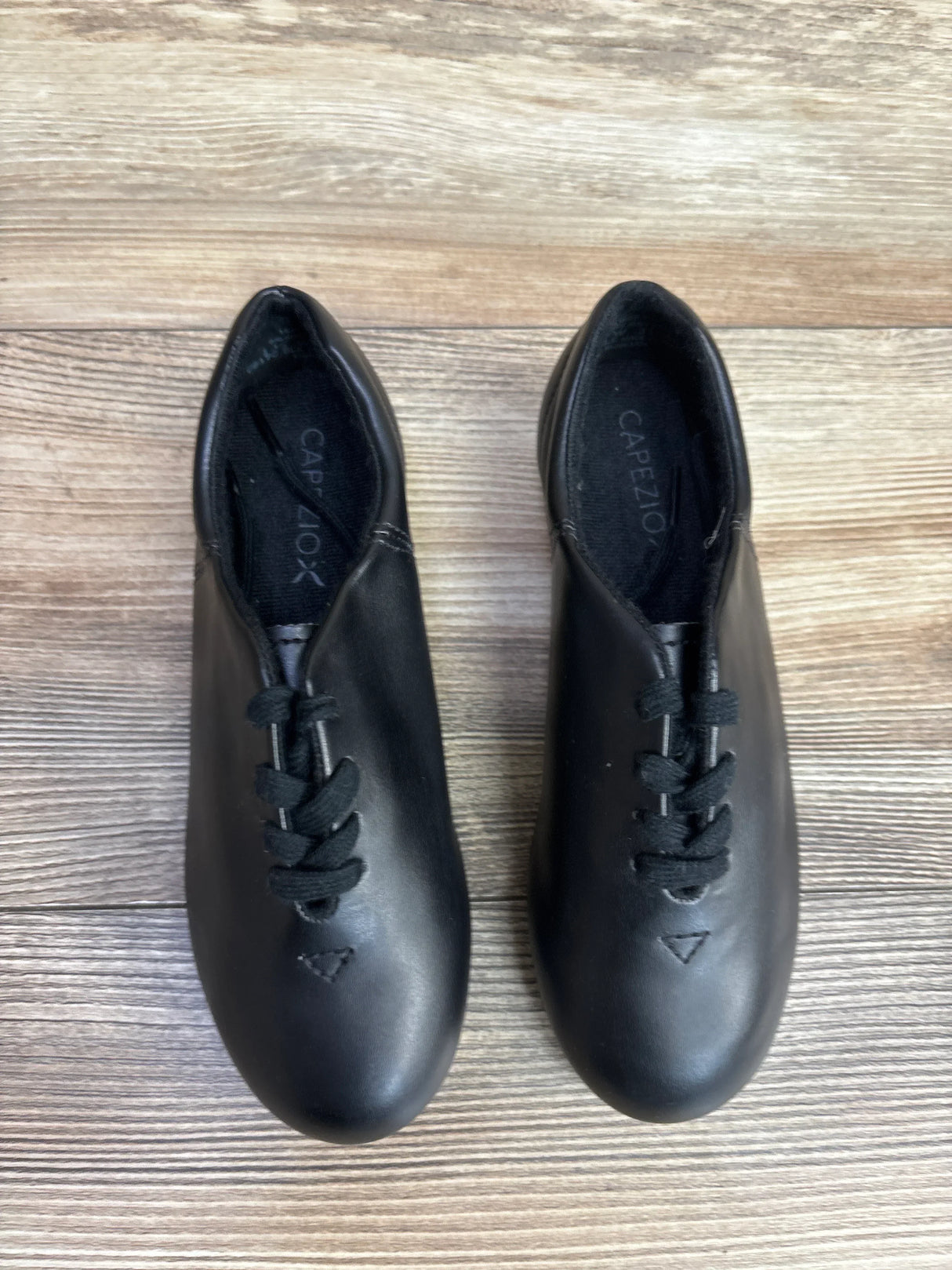 Pair of black Capezio leather jazz dance shoes with laces on wooden floor background