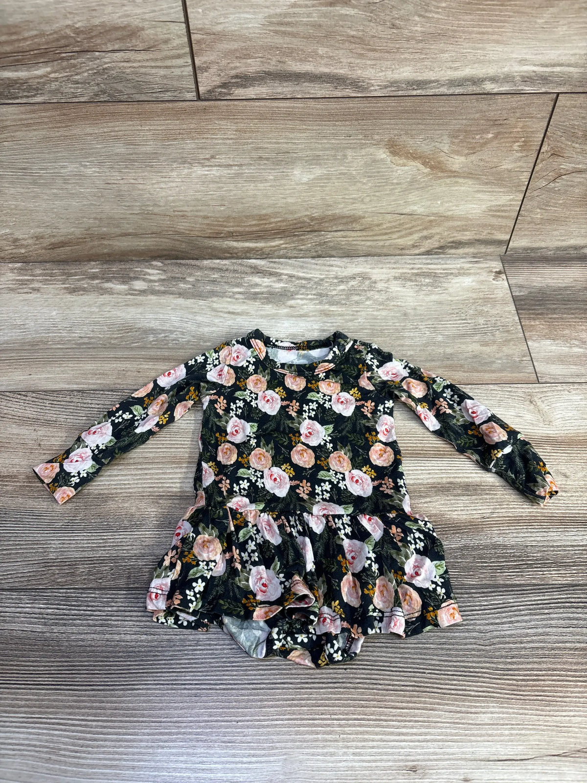 Front view of Gigi & Max black bamboo floral tutu bodysuit showcasing long sleeves and tutu skirt on wood-look flooring