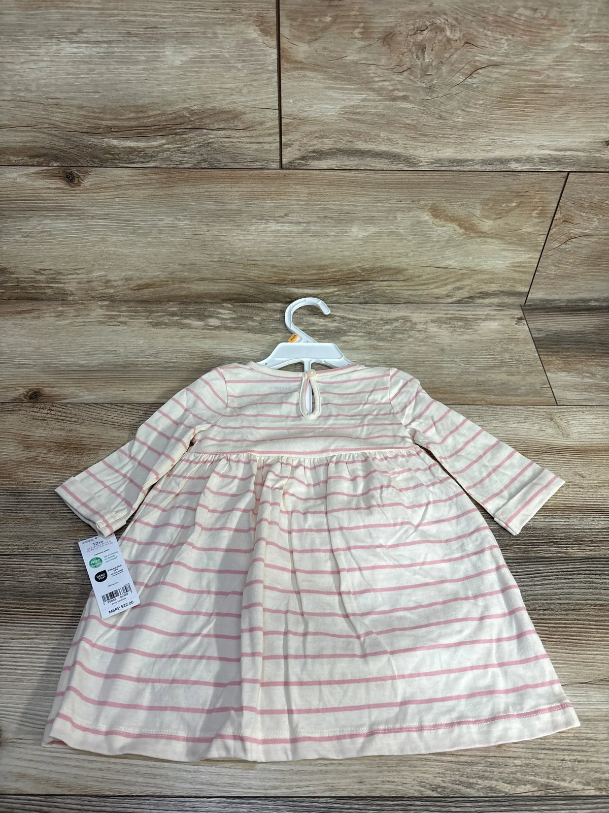 Pink and white striped baby dress with long sleeves on hanger, wood background