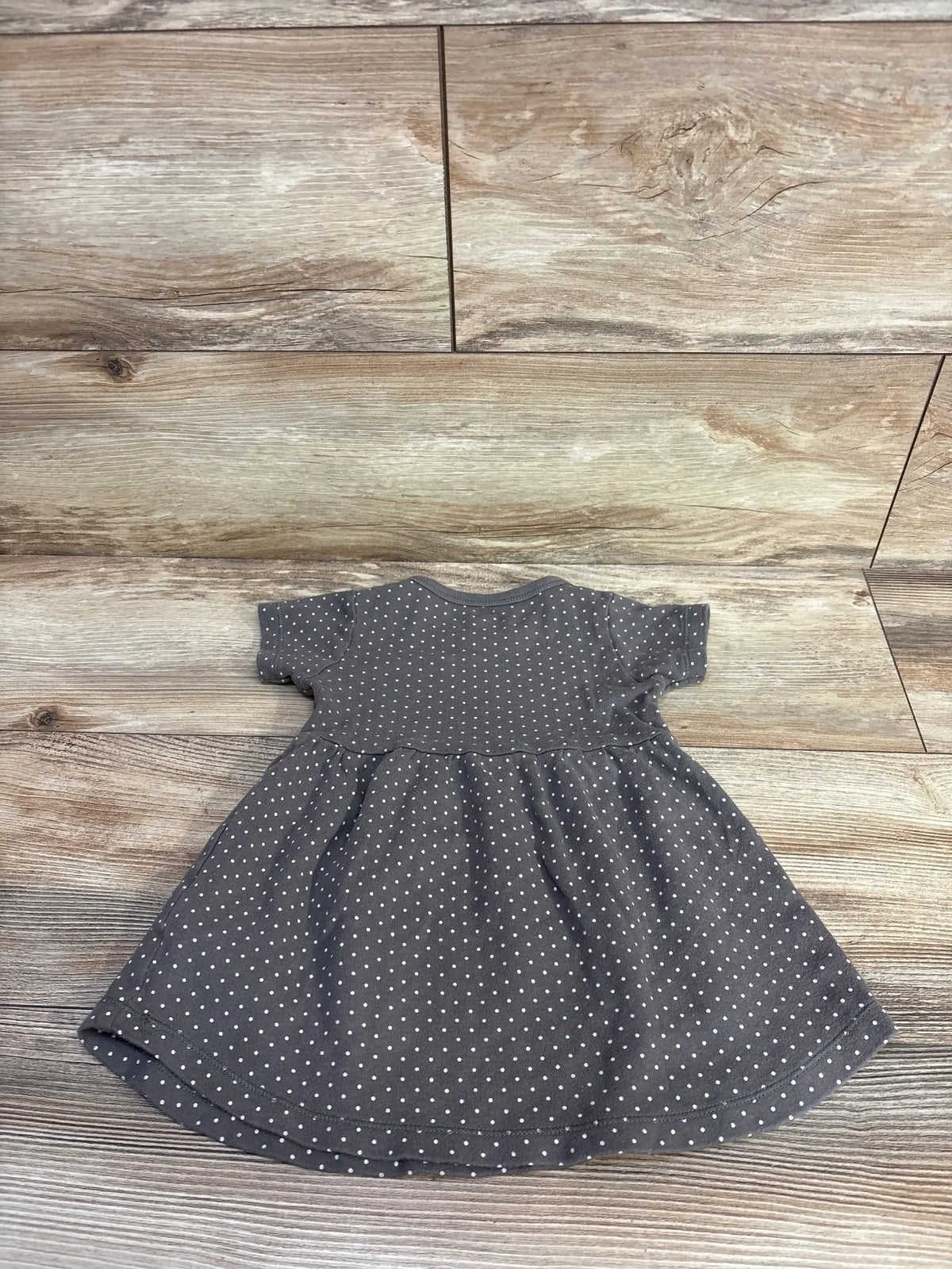 Flat lay of Hudson Baby brown polka dot baby dress showcasing short sleeves and gathered skirt on wooden floor