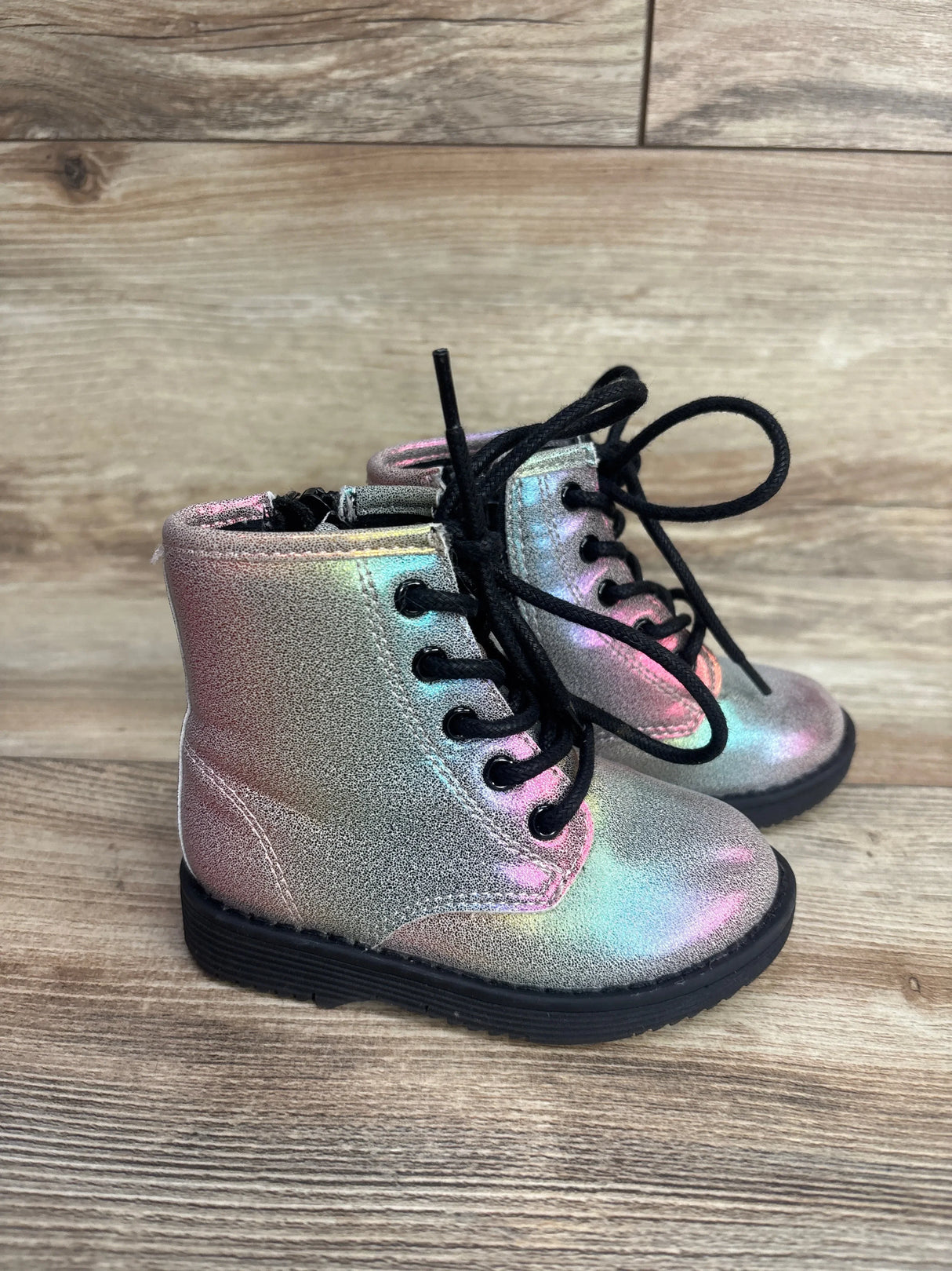 Iridescent toddler lace-up boots with black soles on wood floor