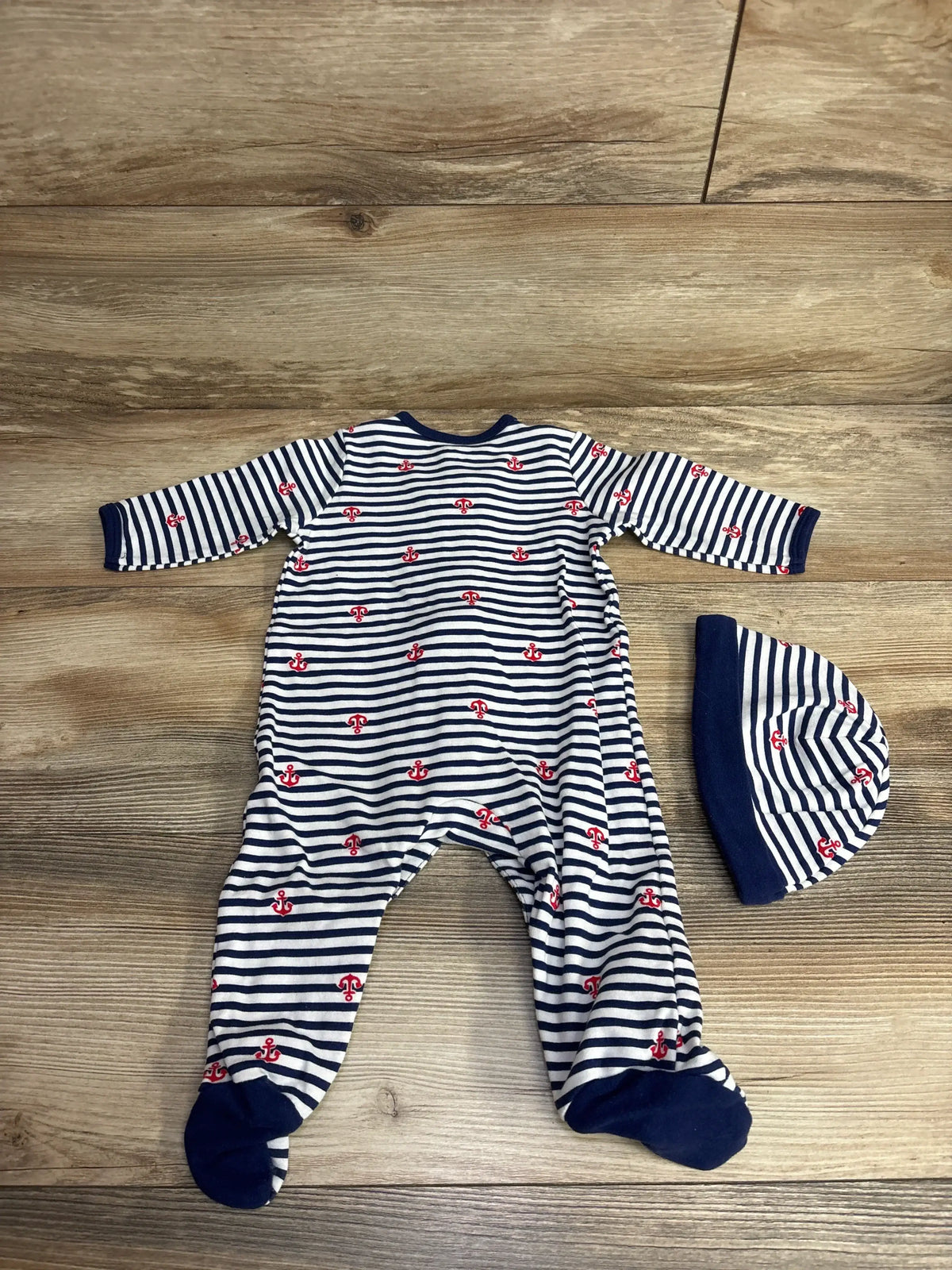 Navy and white striped baby onesie with red anchor patterns and matching hat on wood floor