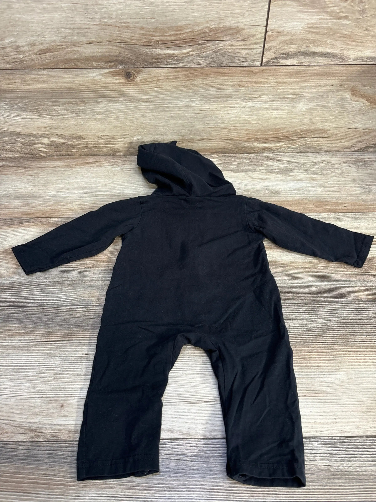 Back view of skeleton hooded coverall (3–6 months) showing attached hood and long sleeves on wood floor background