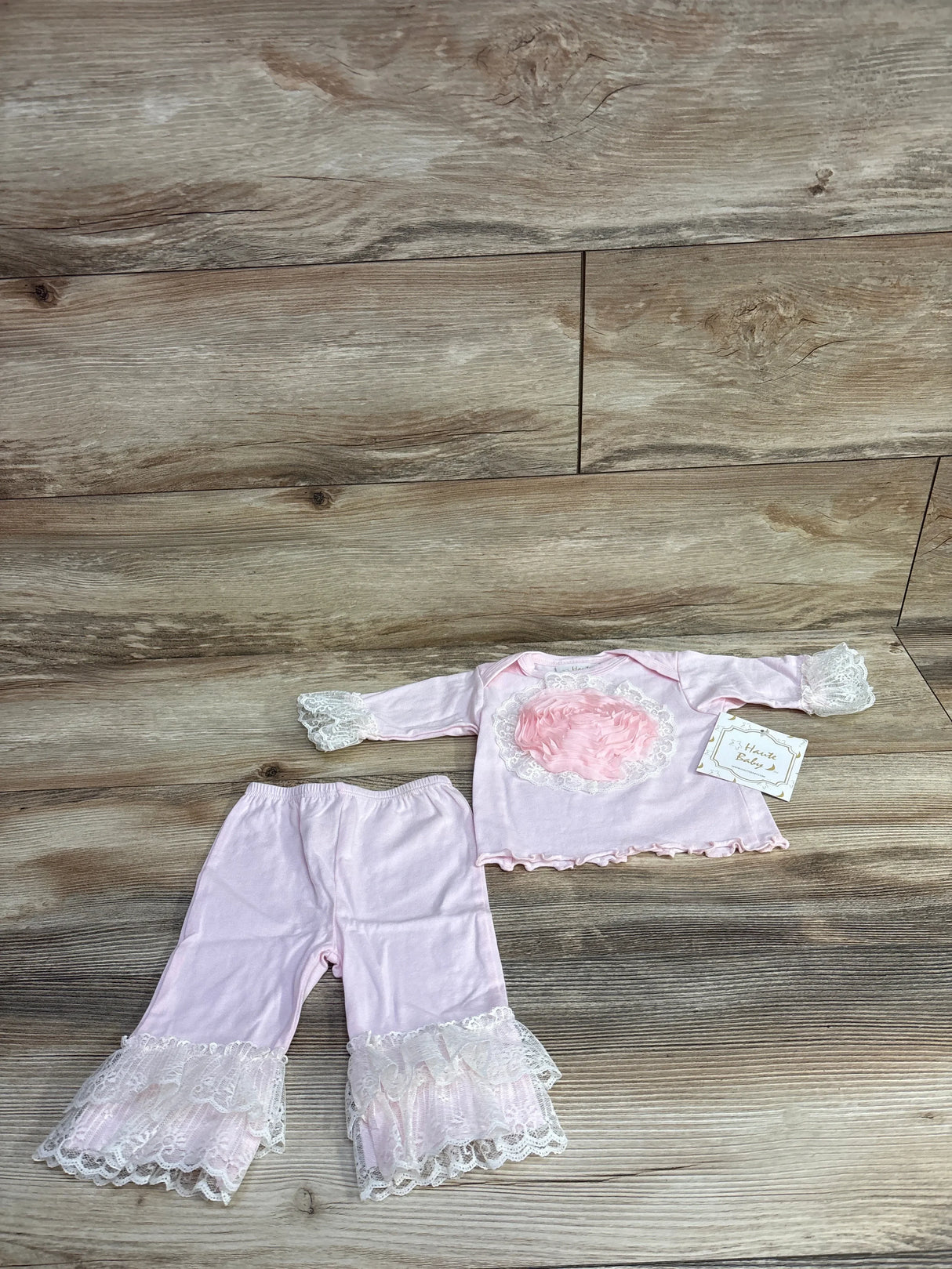 Pink baby girl outfit with lace cuffs and floral decoration, set on wooden surface