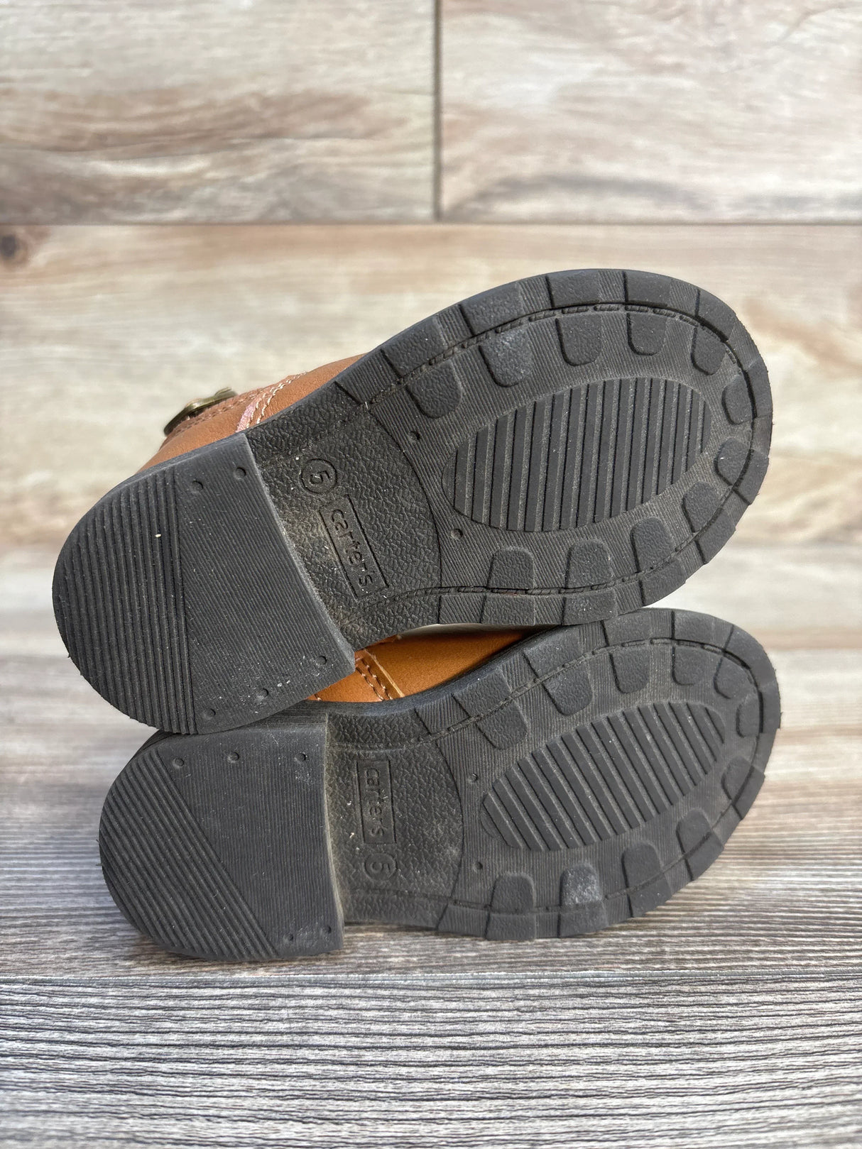 Bottom of toddler brown boots with black rubber soles, size 5, lightly worn, wood background