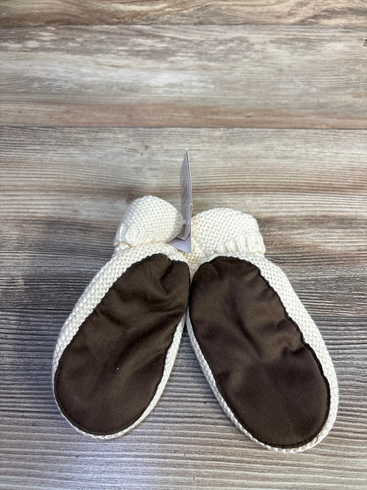 Bottom view of NEW knit booties in cream showcasing dark flexible nylon soles with a wood grain background