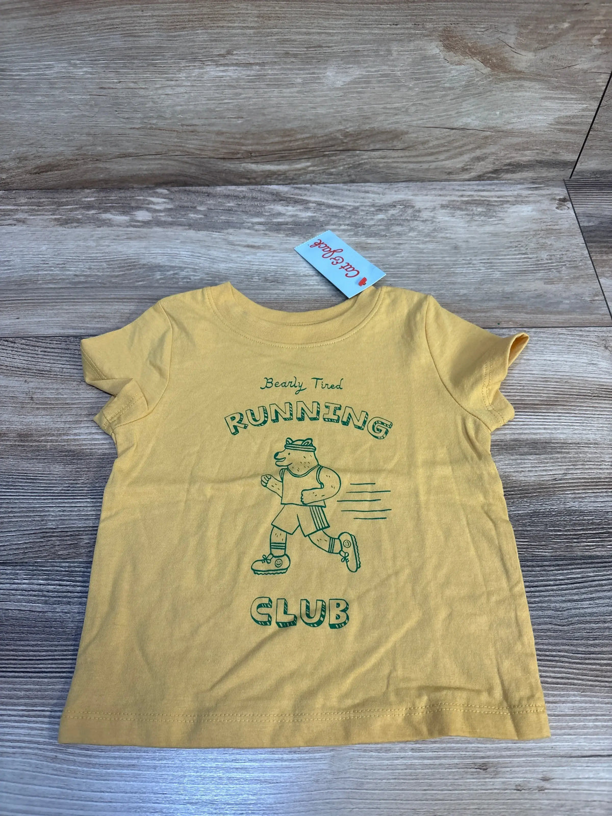 Yellow kids t-shirt with bear cartoon and 'Bearly Tired Running Club' text on wood surface