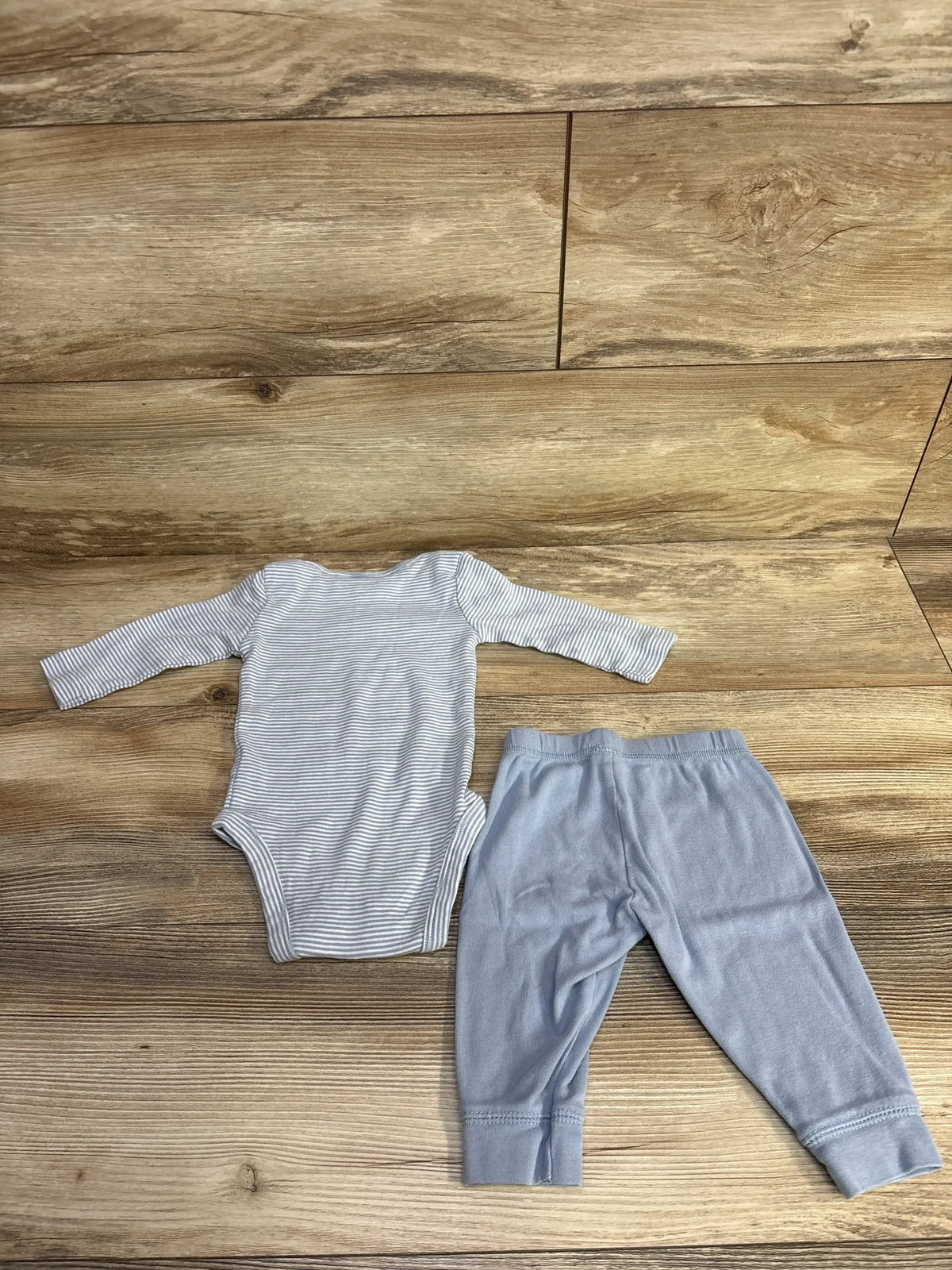 Flat lay of blue striped long-sleeve bodysuit and light blue pants showcasing soft cotton fabric on wood floor background