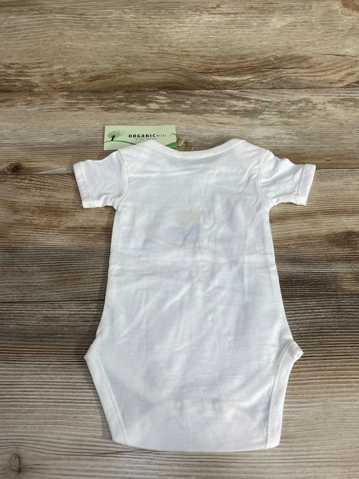 White organic cotton baby onesie laid flat on wooden surface with Organic Hill tag attached