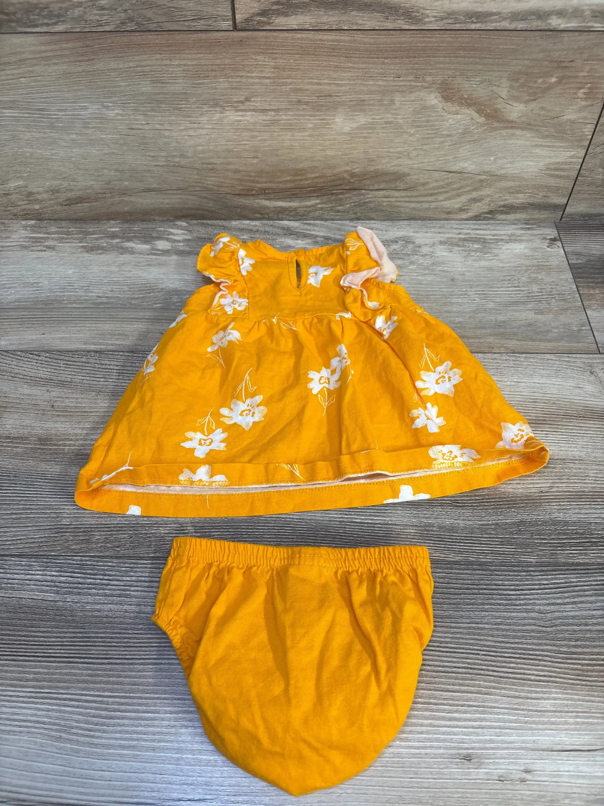 Flat lay of yellow baby dress and matching bloomers showing white floral print and ruffled sleeves on wood floor