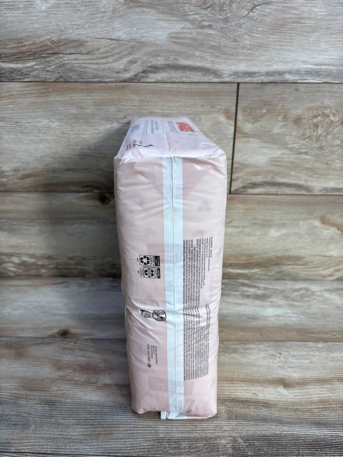 Side view of Huggies Skin Essentials Diapers Size 1 (66 count) showcasing sealed pink retail package on wood floor background