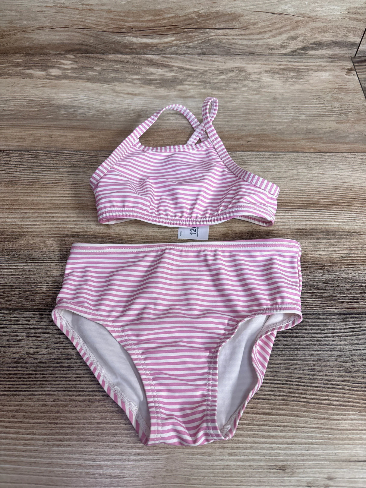 Flat lay of Carters 2pc swimsuit in pink and white stripes showcasing crossback top and high-waist bottoms on wood plank floor