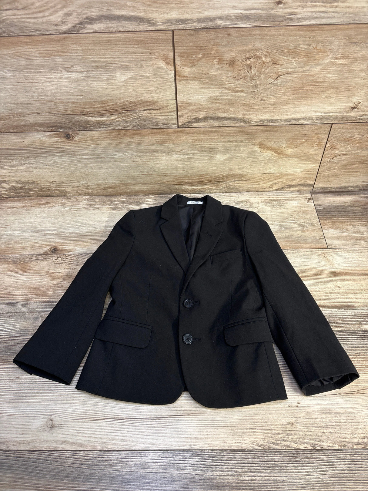 Black formal blazer with two buttons and flap pockets laid flat on wooden floor