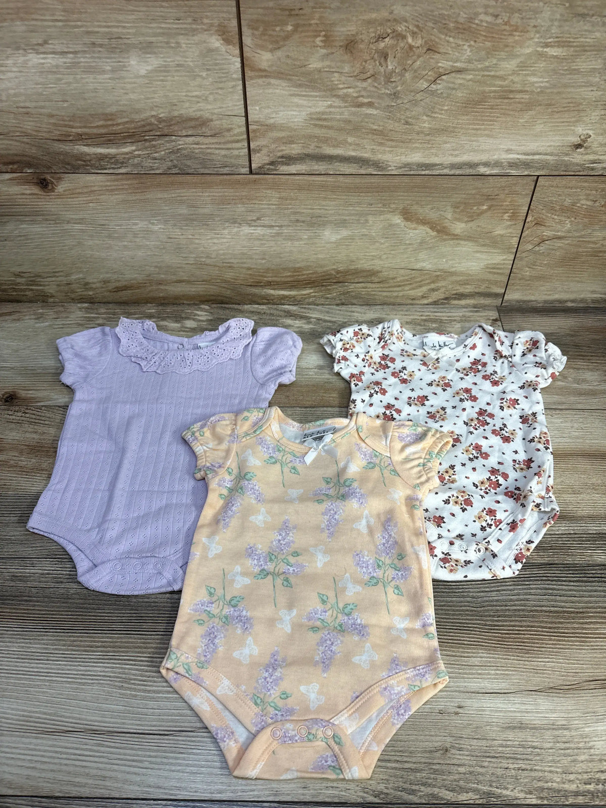 Nicole Miller 3-pack of puff sleeve baby bodysuits in purple, floral white, and yellow floral.