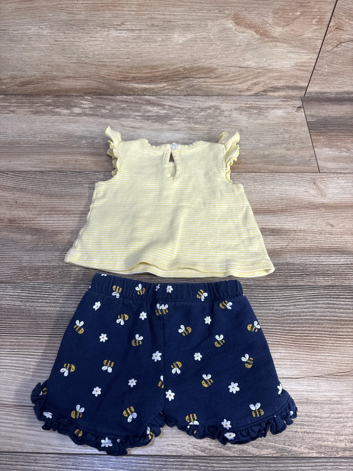 Front view of Little Me 3-month two-piece set showcasing a yellow bee tank top and navy bee-print shorts on wood flooring