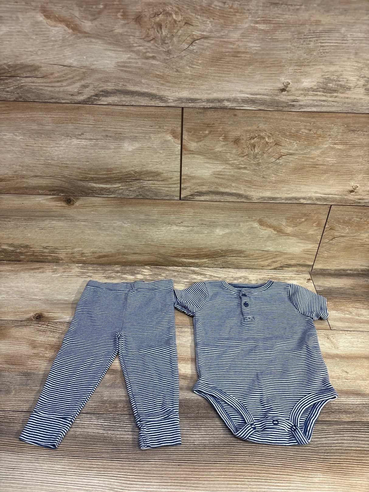 Flat lay of navy-and-white striped henley bodysuit and pants showing henley buttons and crotch snaps on wood background