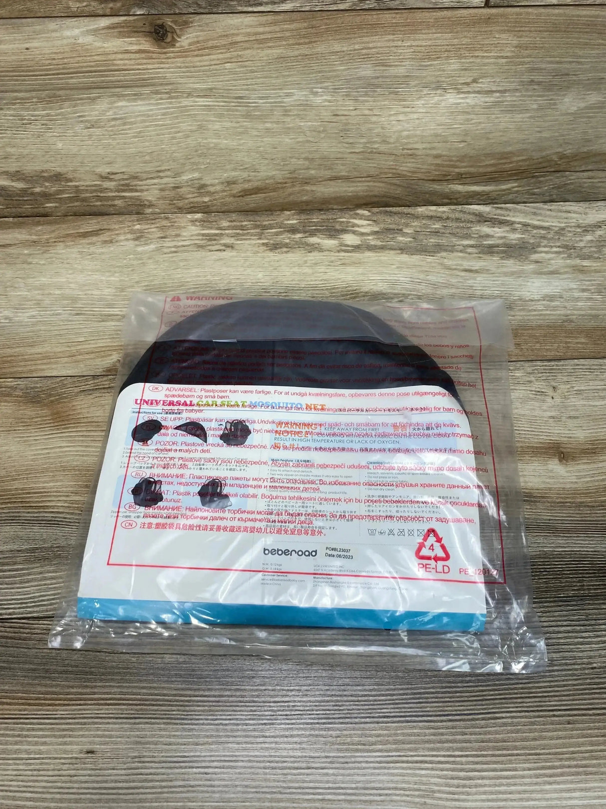 Top-down view of Beberoad Love universal car seat mosquito net in black folded inside clear plastic packaging on wooden tabletop