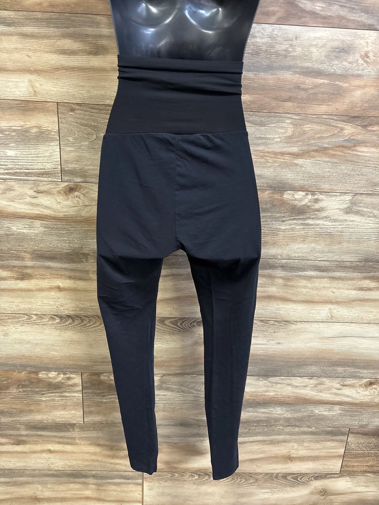 Front view of black maternity full-panel leggings on mannequin showing high-rise belly panel and slim legs against wood background
