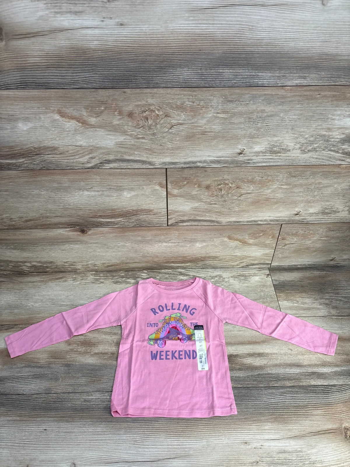 Pink toddler long sleeve shirt with roller skate graphic and 'Rolling into the Weekend' text on wood floor