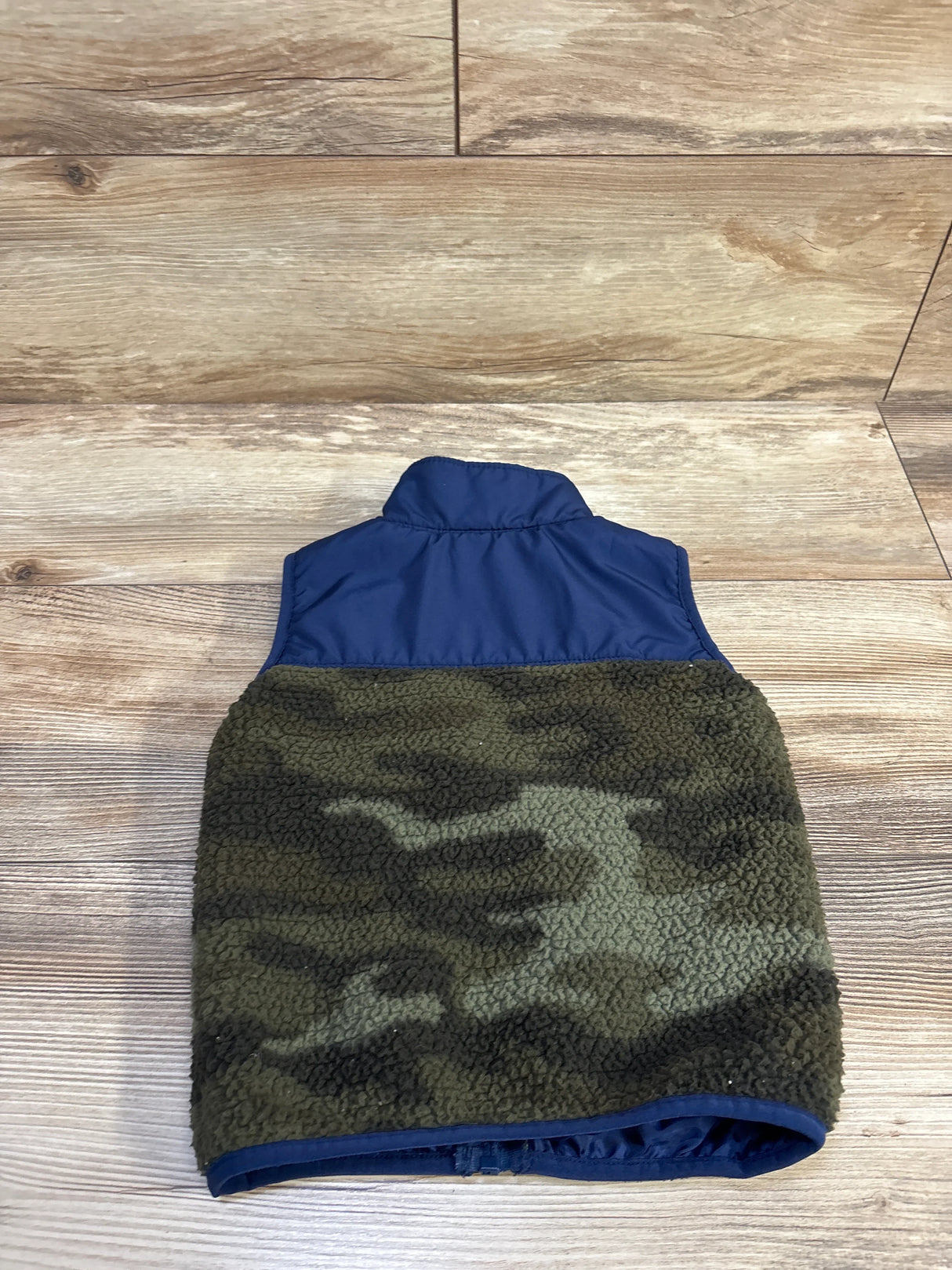 Back view of toddler sherpa full-zip vest showcasing navy nylon yoke and camo green sherpa body on light wood floor