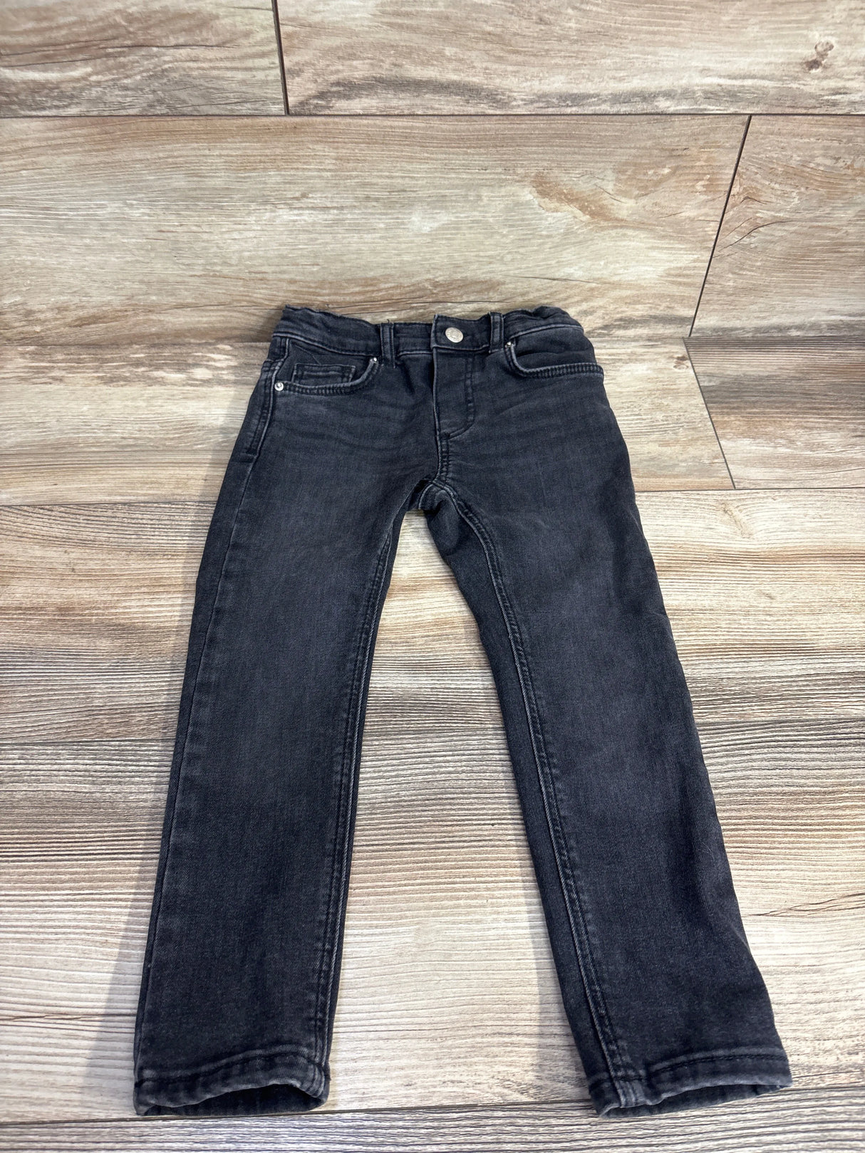 Black denim kids jeans with button closure laid flat on wooden floor