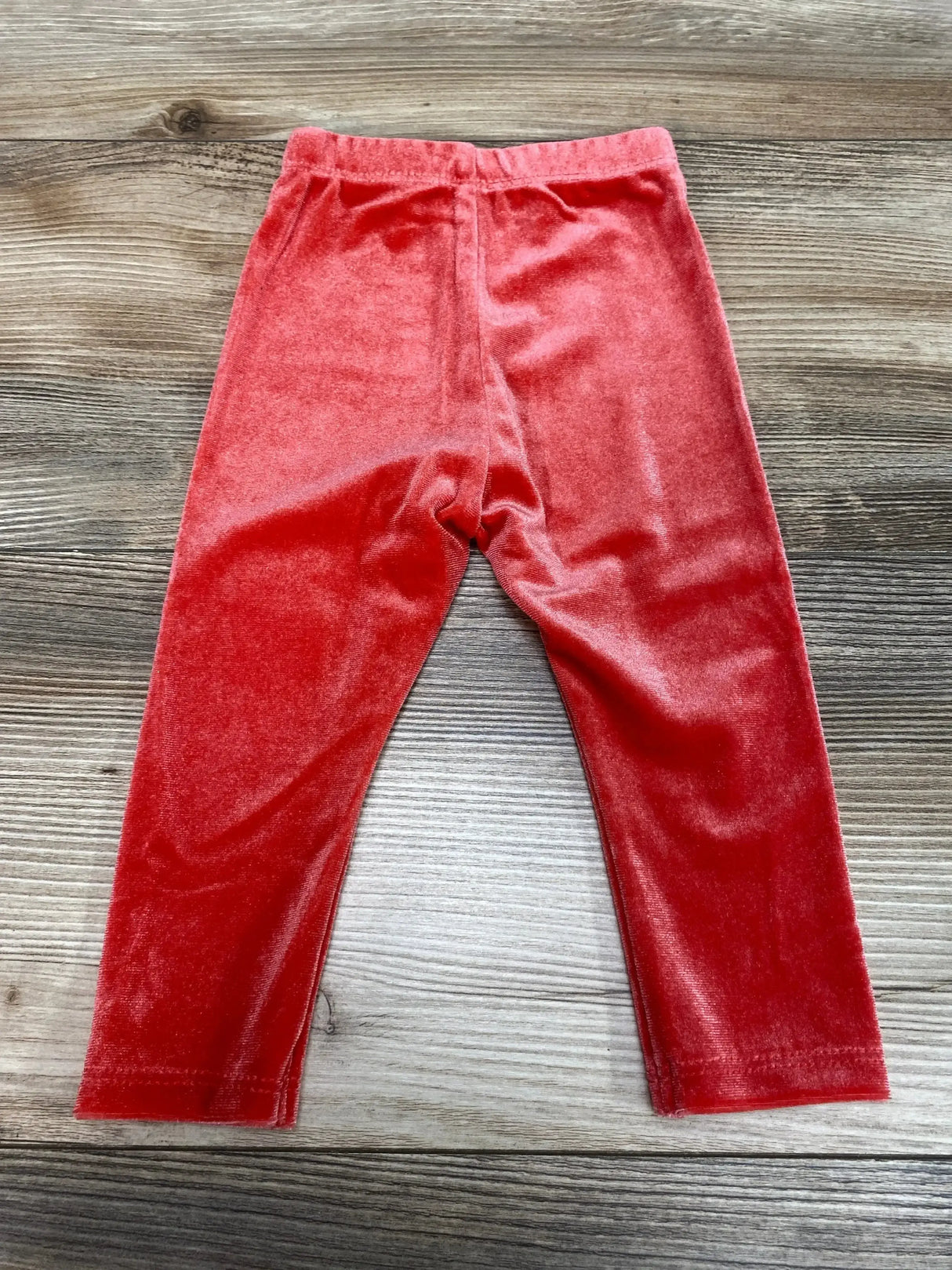 Flat lay of Okie Dokie velour baby leggings in Tokyo red, size 6 months, showing elastic waistband and soft plush texture on wood background