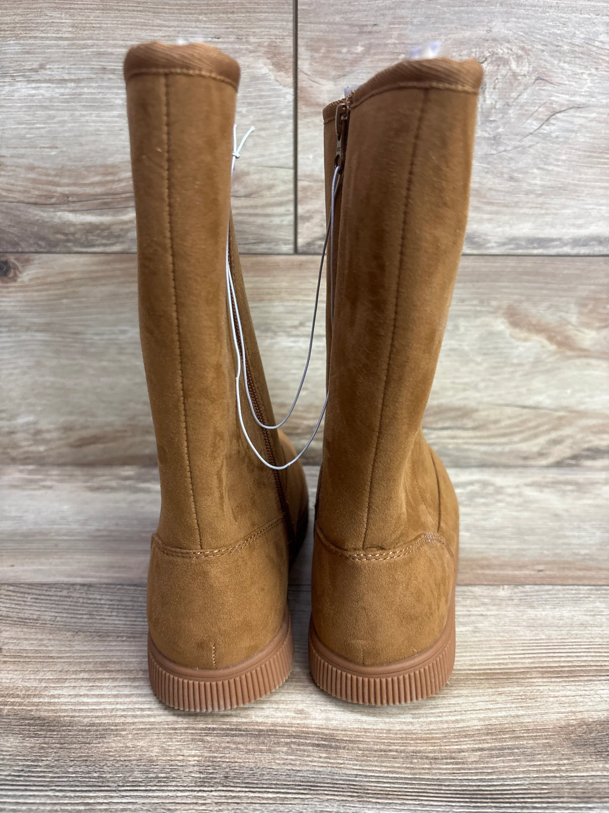 Pair of tan suede kids' boots with zippers, displayed on wooden floor and background