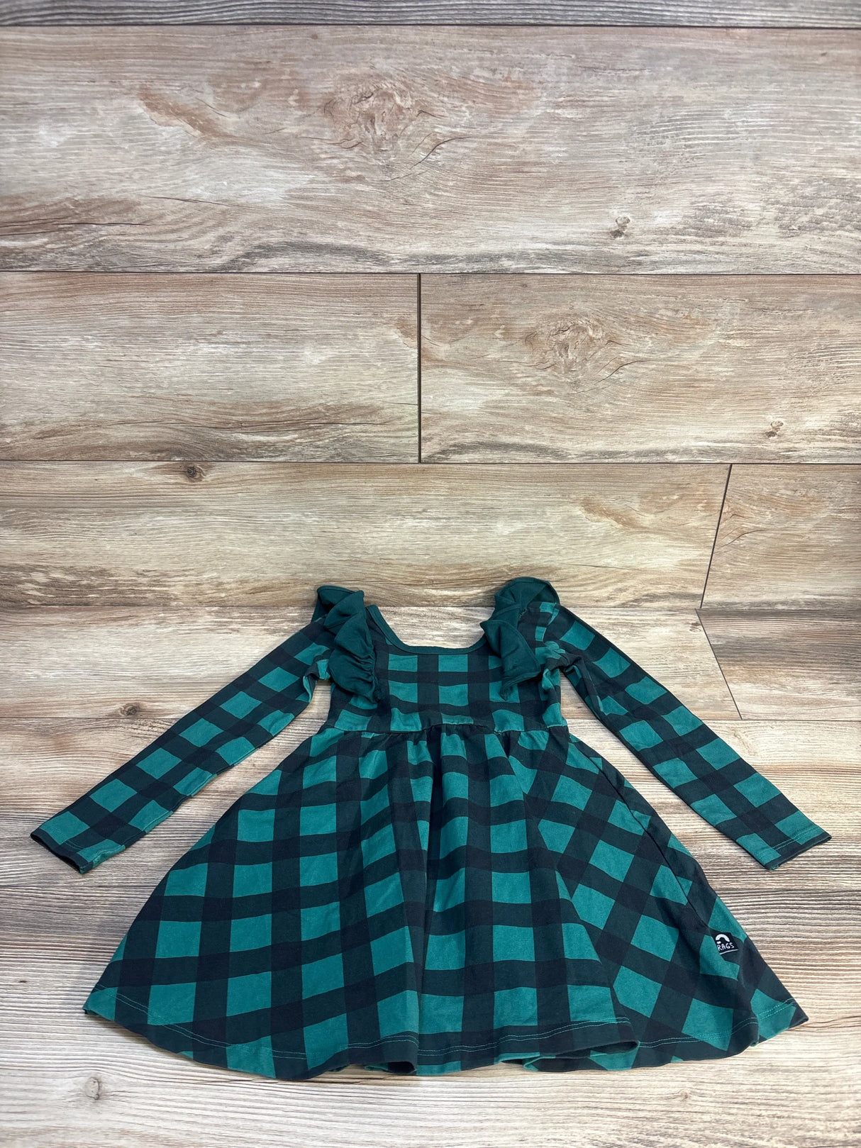 Green and black plaid long sleeve girls dress with ruffle shoulders on wooden floor