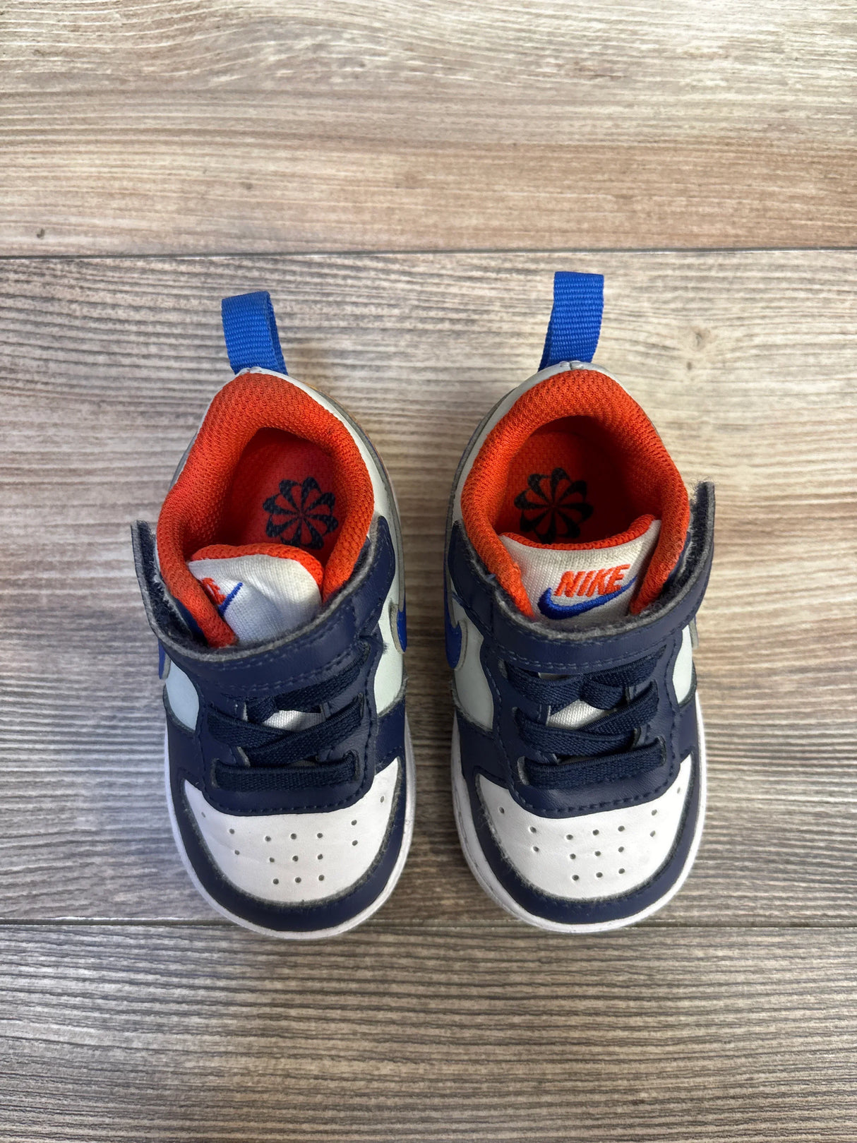 Navy blue and white Nike toddler sneakers with orange lining on wood floor