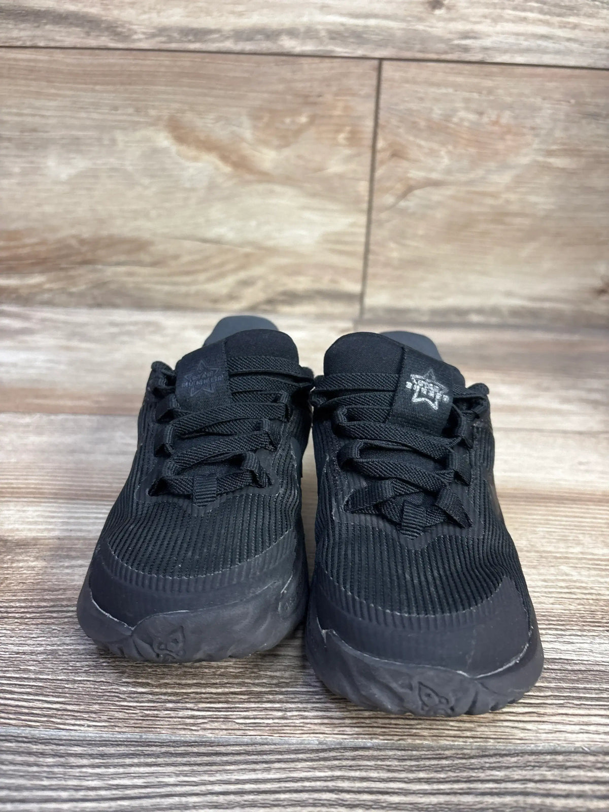 Front view of Nike Star Runner 4 TD toddler sneakers showing triple black ribbed upper and laces on a wood floor backdrop