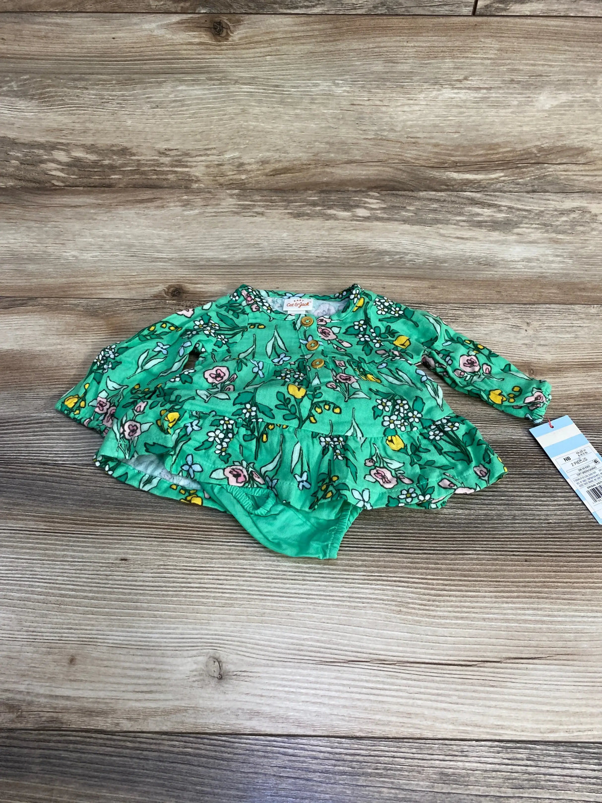 Flat lay of newborn green floral Henley dress with matching bloomers showing front buttons and ruffled skirt on wood background