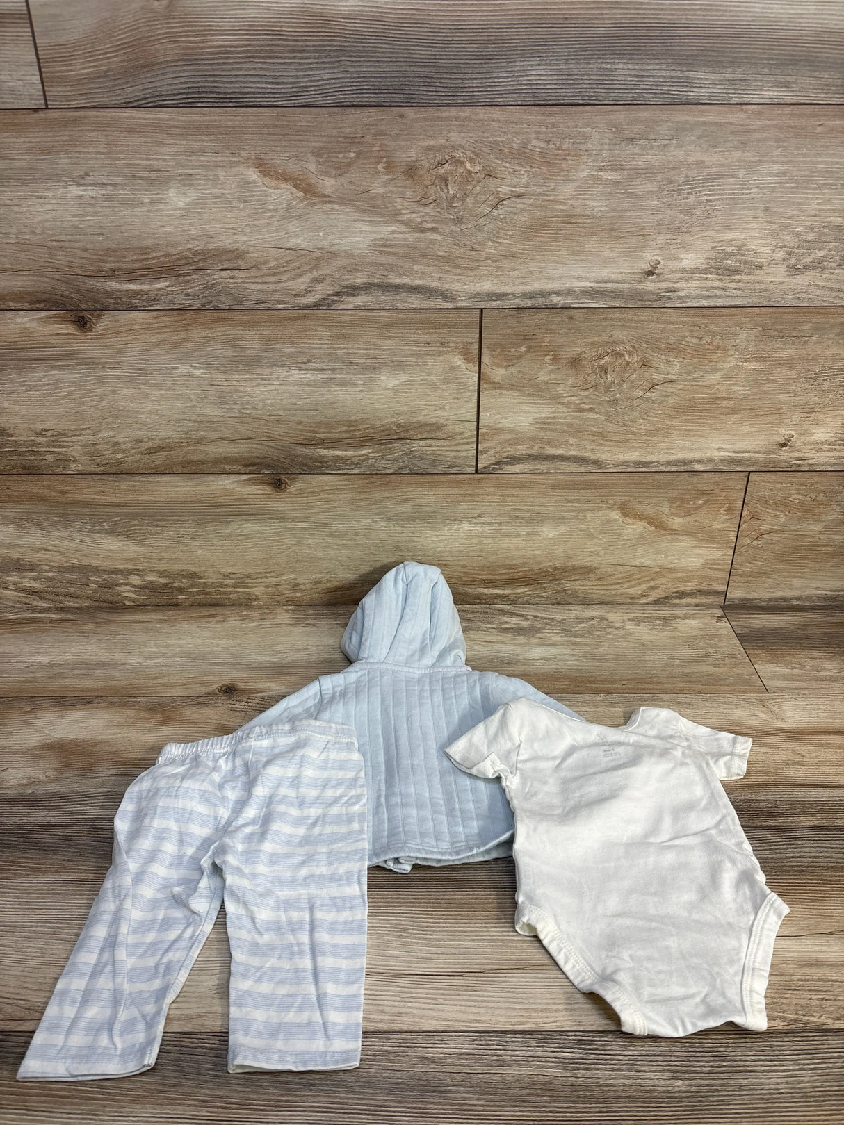 Baby boy clothing set: striped hoodie, pants, and white onesie on wood floor
