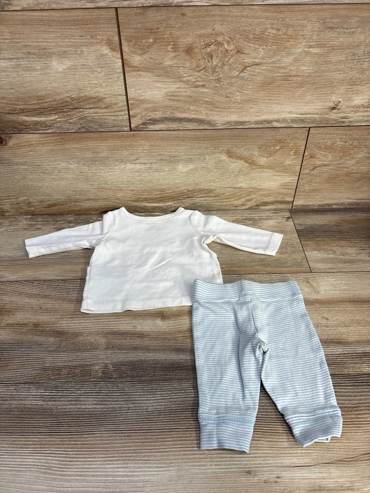 Top view of Carter’s shirt and pants set showcasing a white long-sleeve shirt and light blue striped pants on a wood floor