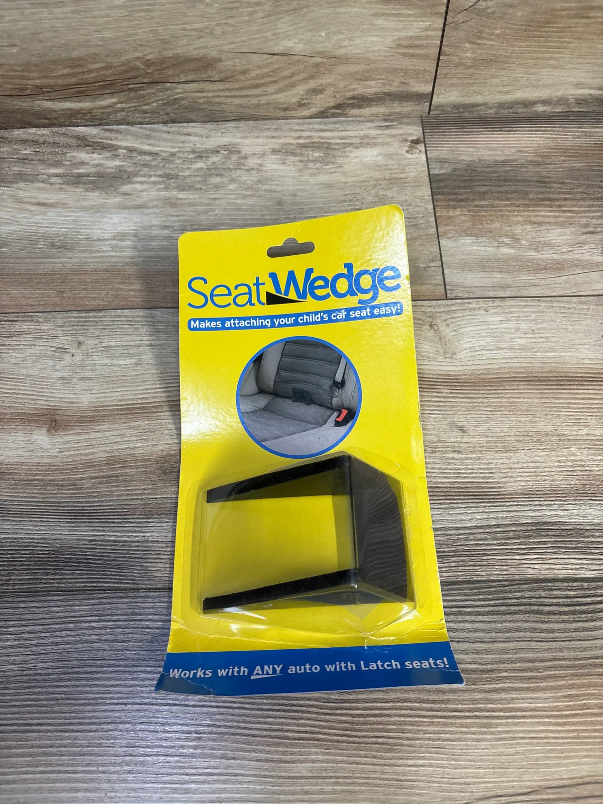 Top-down view of SeatWedge car seat wedge showcasing the black wedge in yellow retail packaging on wood floor