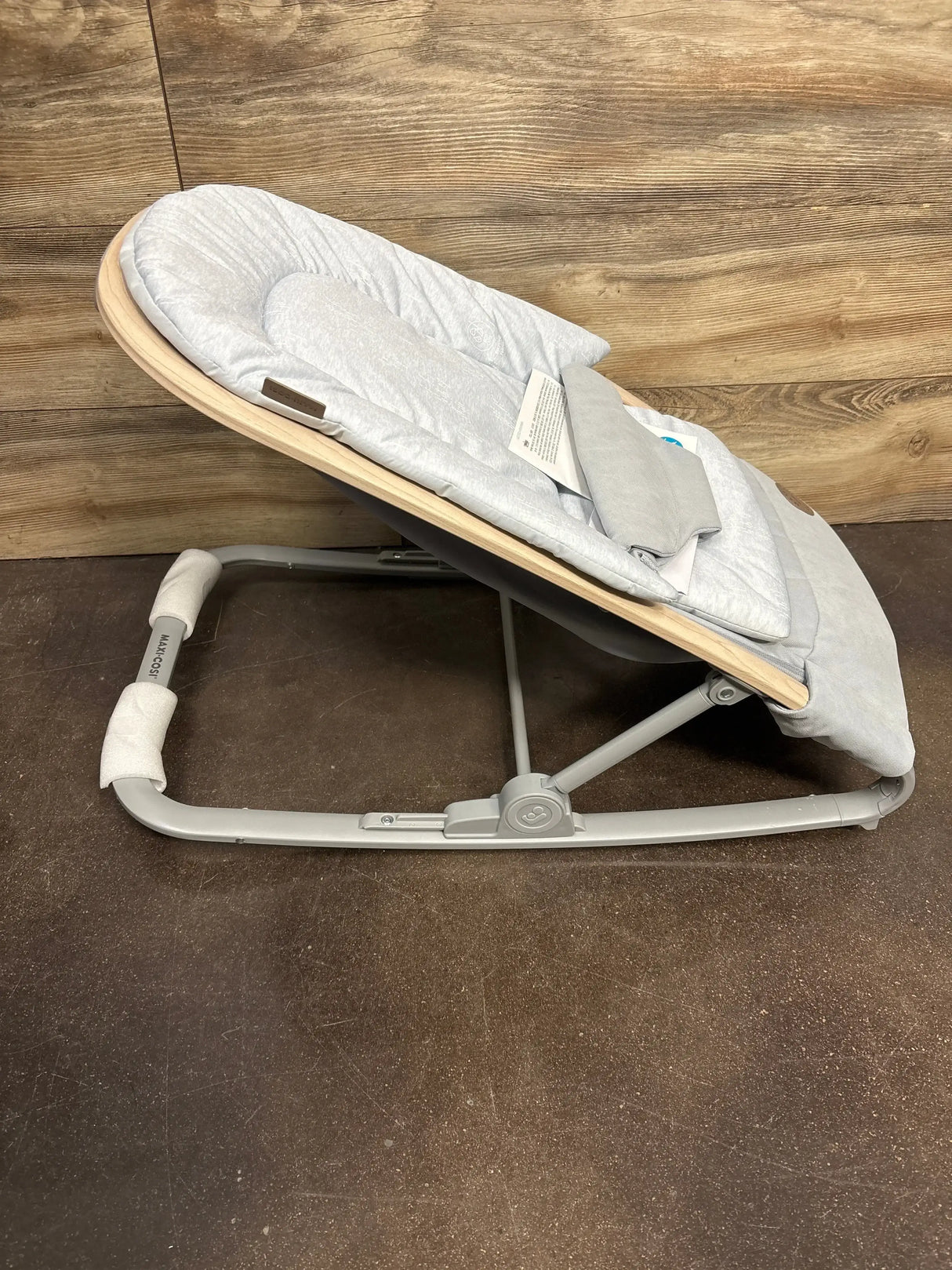 Side view of Maxi-Cosi Kori 2-in-1 baby rocker with quilted light gray seat and wood-effect shell on brown floor