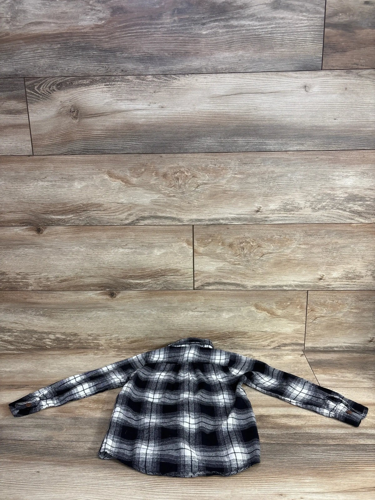 Black and white plaid long-sleeve kids shirt on wooden floor background from children's resale store