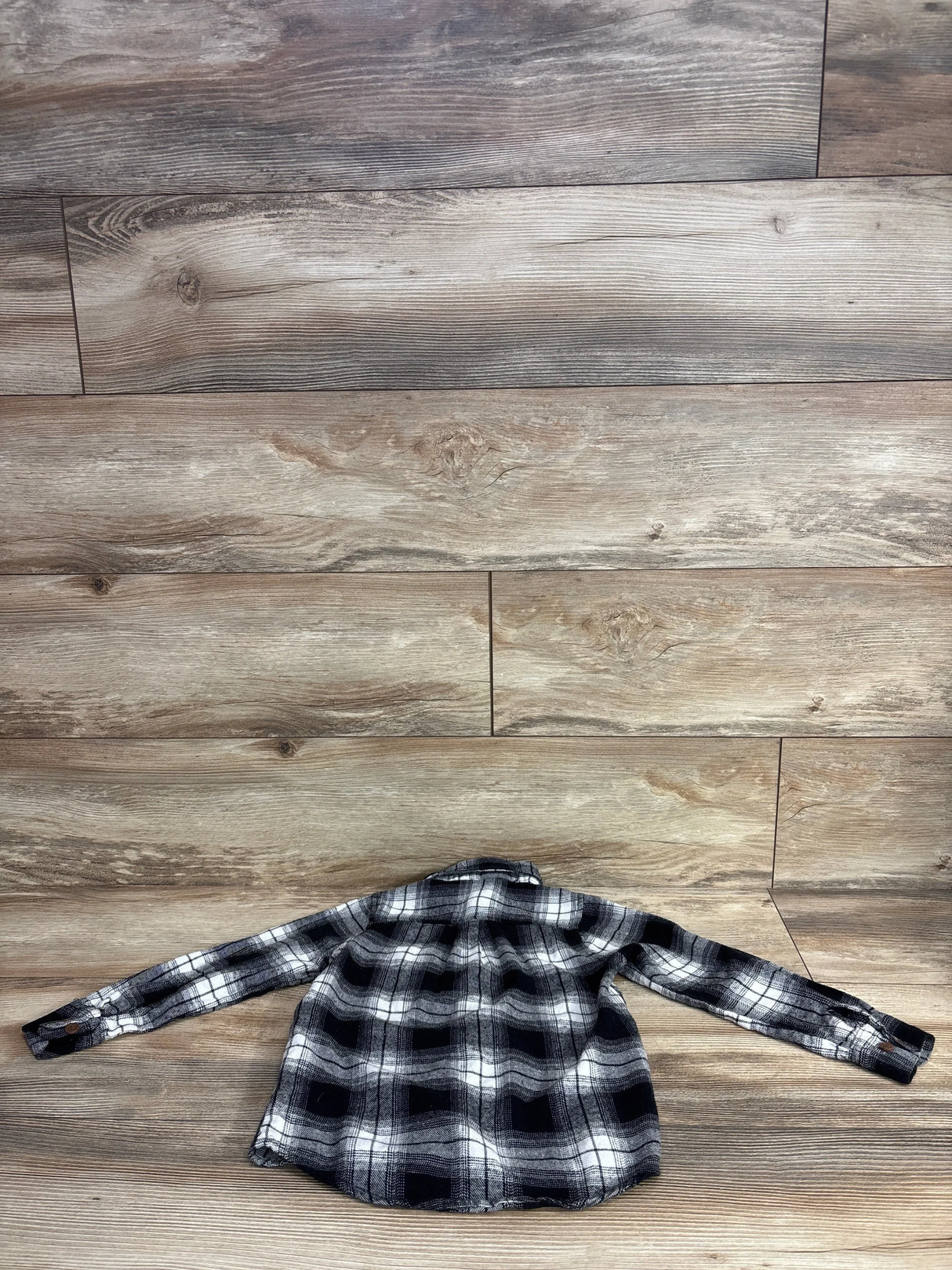 Black and white plaid long-sleeve kids shirt on wooden floor background from children's resale store