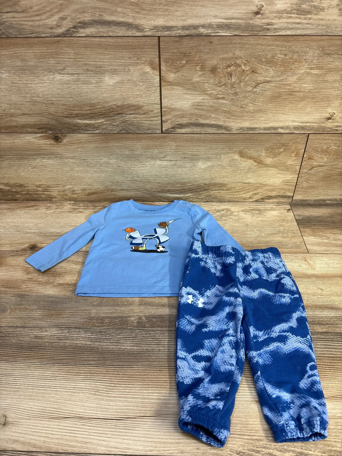 Flat lay of Under Armour blue long-sleeve shirt and pants set showcasing a graphic shirt and camouflage pants on wood floor