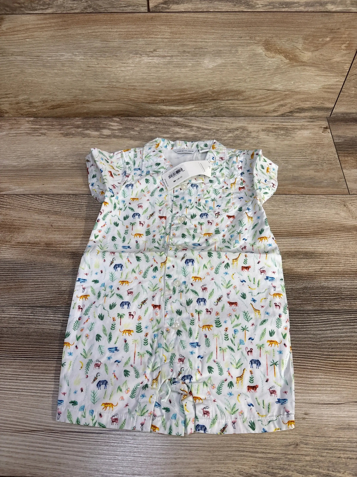 Flat lay of NWT Janie and Jack jungle print shortie romper white size 6-12m showcasing multicolor jungle animal print and flutter sleeves on wood plank floor