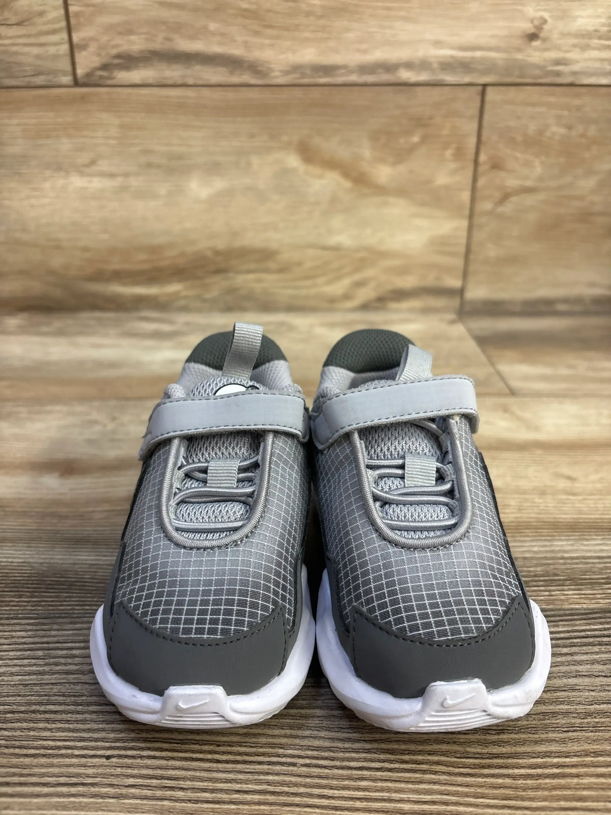 Front view of Nike Air Max Nova TD Wolf Grey toddler sneakers showcasing hook-and-loop straps on a wood floor