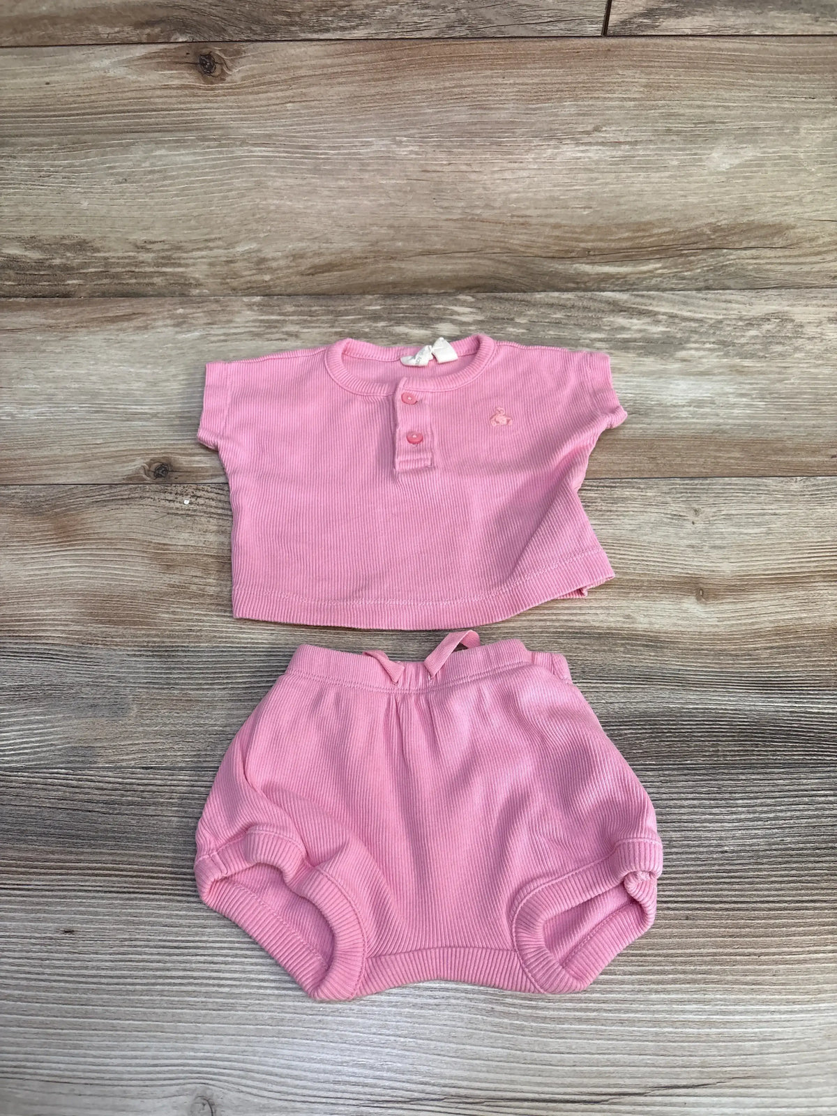 Front view of a pink Baby Gap two piece ribbed Henley top and bloomer shorts with button placket and drawstring waist on wood