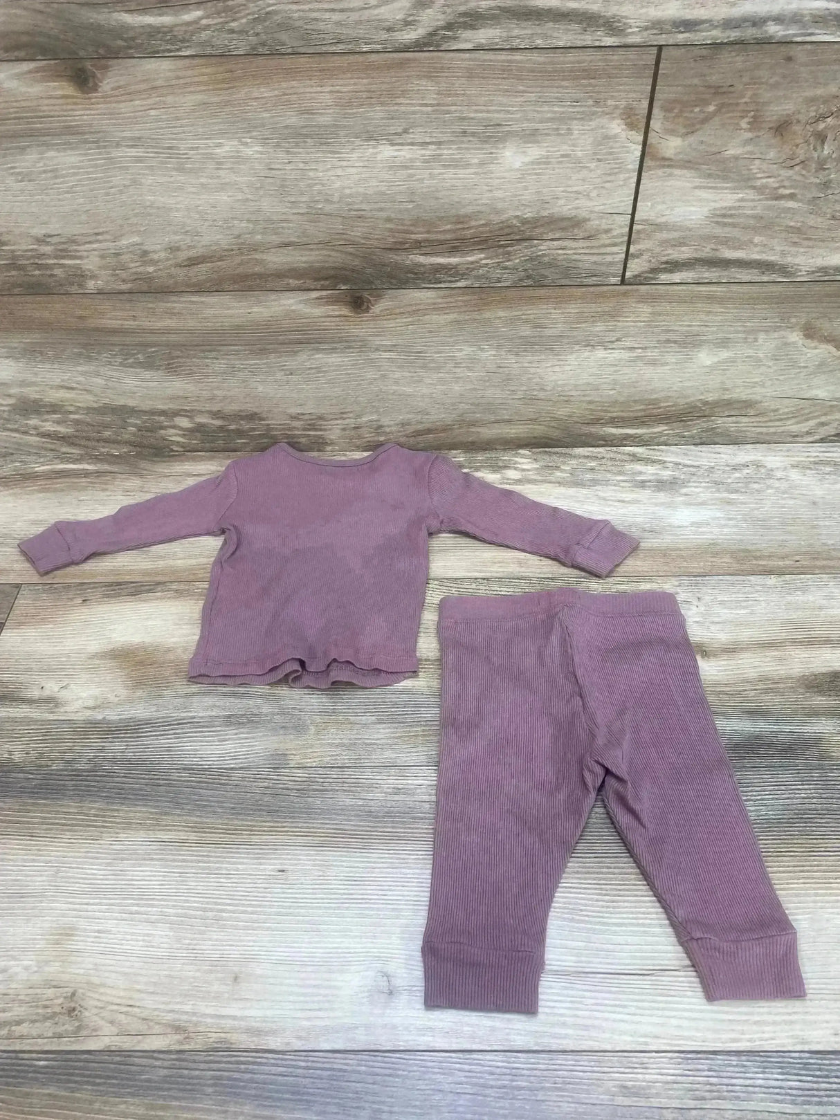 Flat lay of impidimpi ribbed long-sleeve baby shirt and matching pants, mauve purple, size 3 months on wood floor