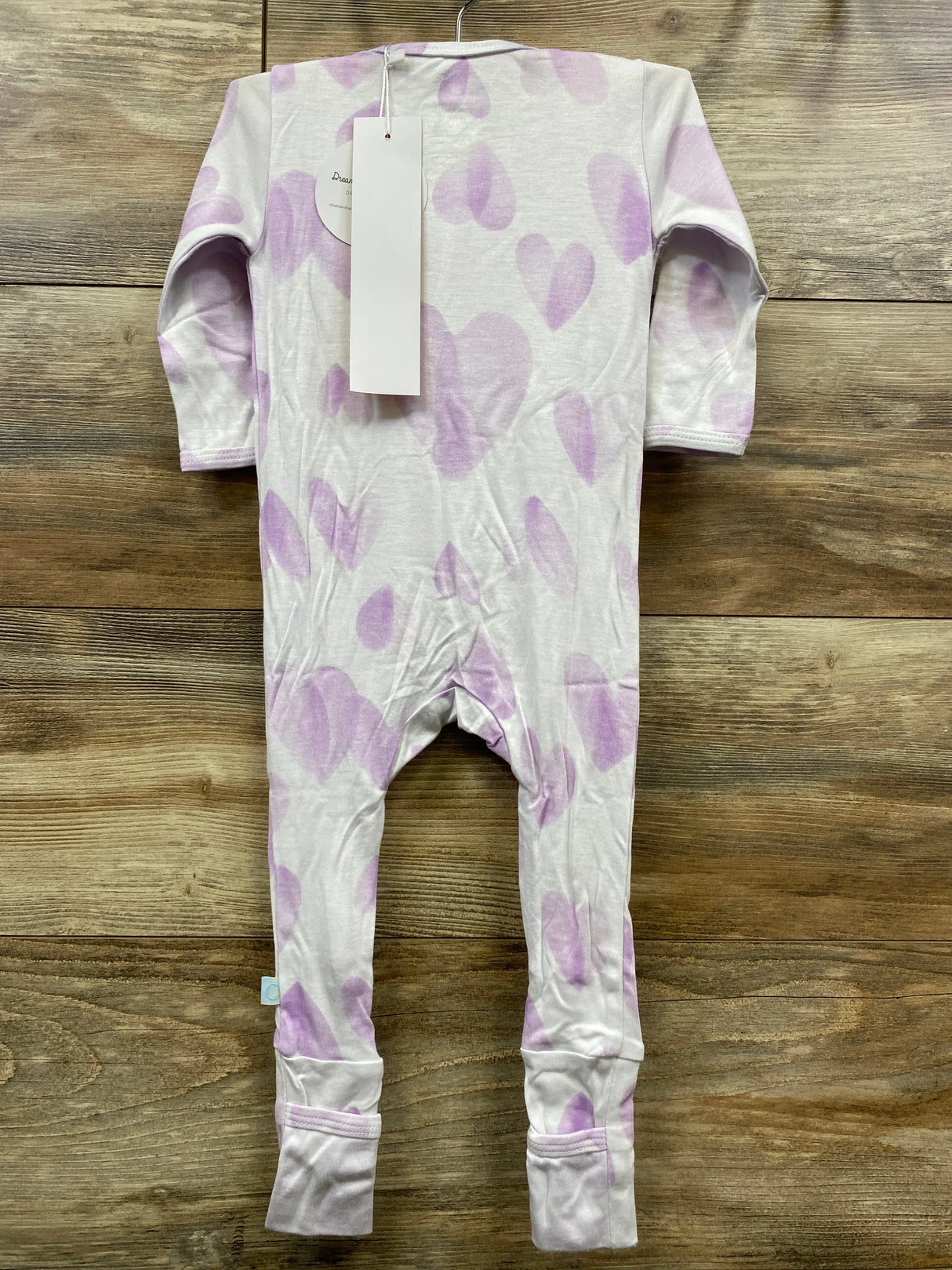 Baby sleeper with purple heart print on white fabric, long sleeves, laid on wood background