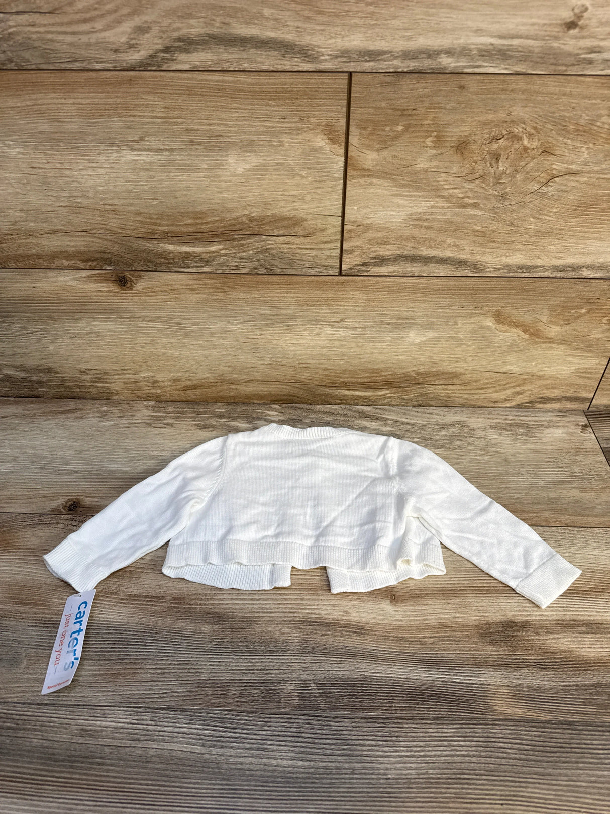 White Carter's baby cardigan sweater with tag on wood background