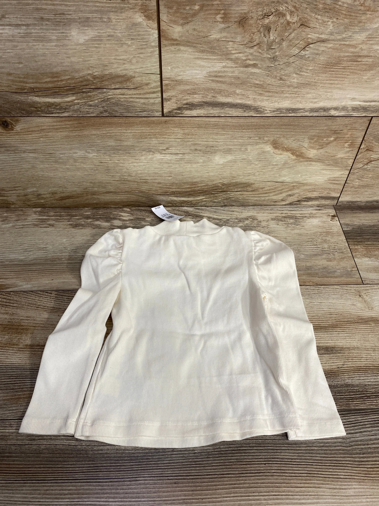 Cream long sleeve ribbed kids shirt with ruffle shoulders on wooden background