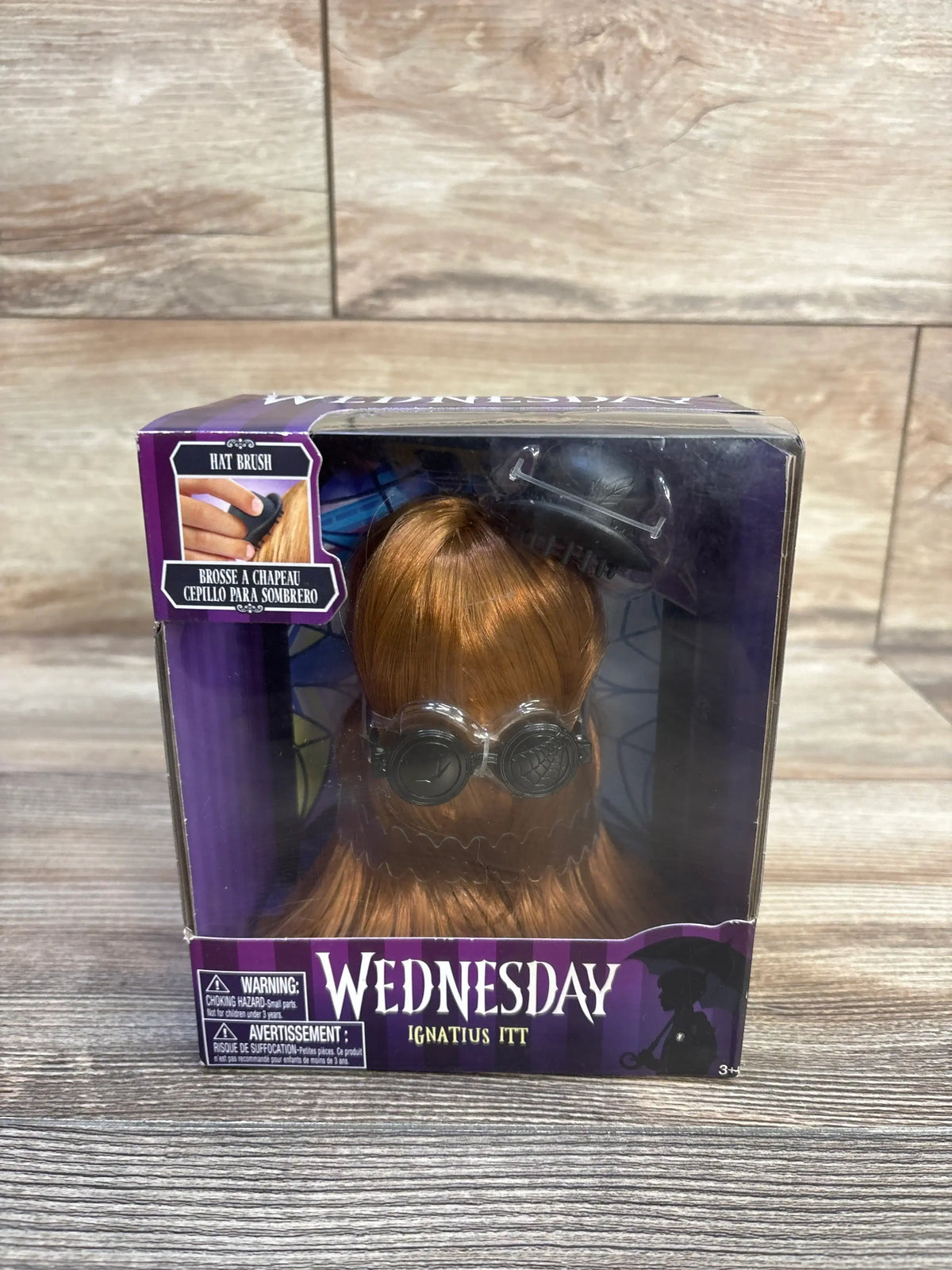 Front view of Ignatius Itt 10-inch styling head in purple Wednesday box showing reddish hair and goggles on wooden tabletop